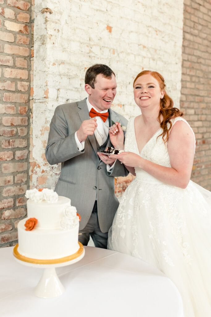 Bride, in white dress, cuts white wedding cake with groom, in grey suit,  at Providence Cotton Mill wedding venue. Photographed by Charlotte wedding photographer, Stephanie Bailey Photography.