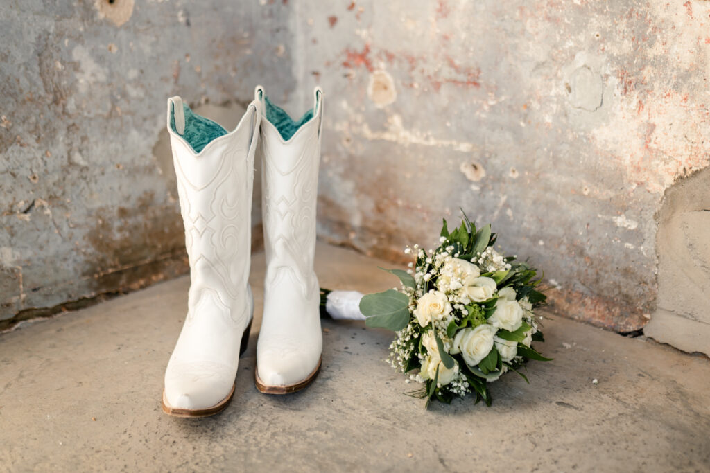 White and blue cowboy boots lay on the floor with white and green wedding bouquet at Providence Cotton Mill wedding venue. Photographed by Charlotte wedding photographer, Stephanie Bailey Photography.