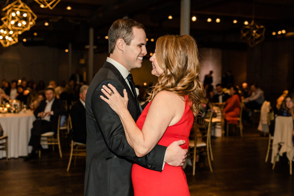 Groom, in black suit, dances with his mom, in a red dress, at Byron's South End wedding venue. Photographed by Charlotte wedding photographer, Stephanie Bailey Photography.