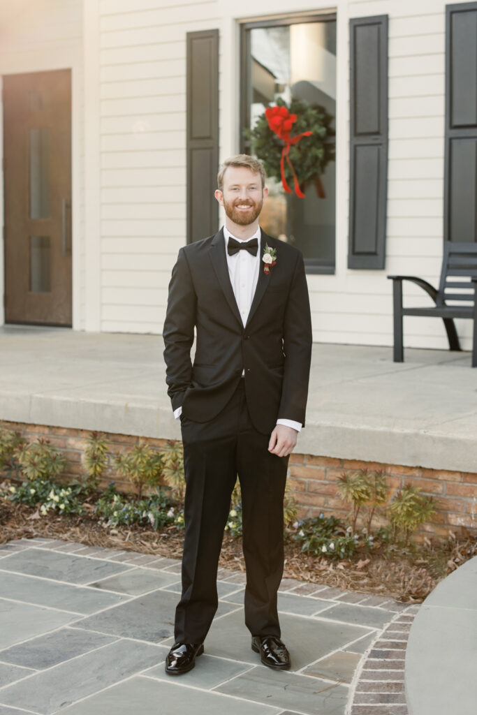 Groom, in black suit and tie, has right hand in pant pocket smiling at 1705 East Raleigh Wedding Venue. Photographed by Charlotte Wedding Photographer, Stephanie Bailey Photography.