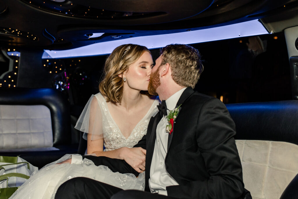 Bride, in white dress, kisses her groom, in black suite and bow tie, in a limo at 1705 East Raleigh Wedding Venue. Photographed by Charlotte Wedding Photographer, Stephanie Bailey Photography.