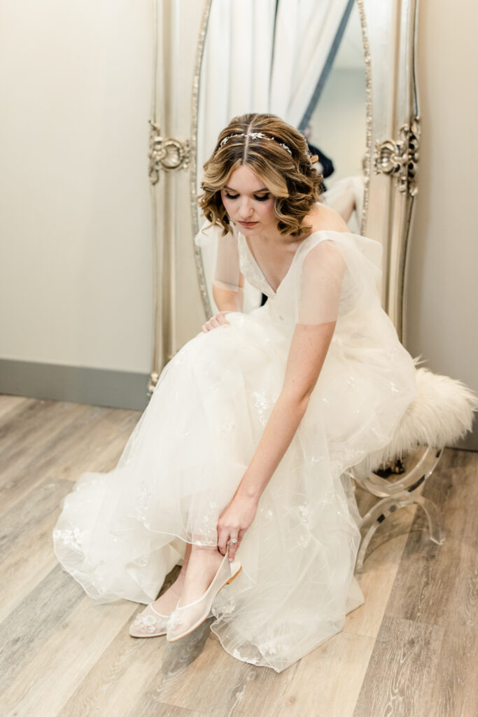 Bride, in white gown, putting on her white shoes at 1705 East Raleigh Wedding Venue. Photographed by Charlotte Wedding Photographer, Stephanie Bailey Photography.