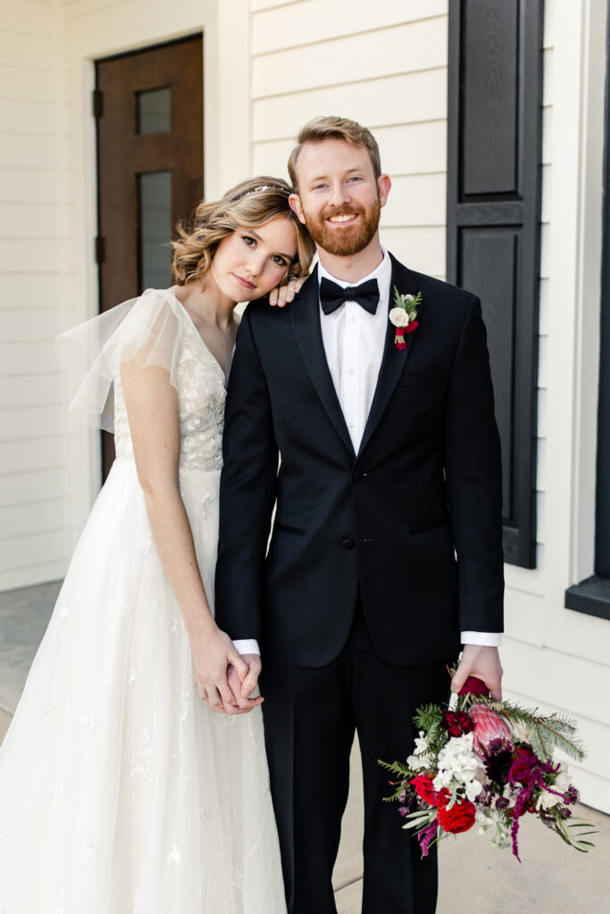 Bride, in white dress, holding hands with groom, in black suit with red floral boutonnière at 1705 East Raleigh Wedding Venue. Photographed by Charlotte Wedding Photographer, Stephanie Bailey Photography.