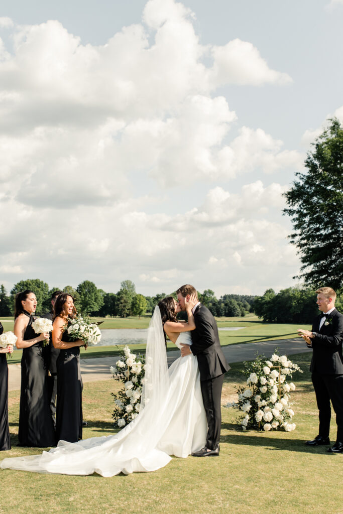 Bride, in white dress and veil, kissing her groom, in black suit, during ceremony on golf course at Long View Country Club Wedding Venue Charlotte NC