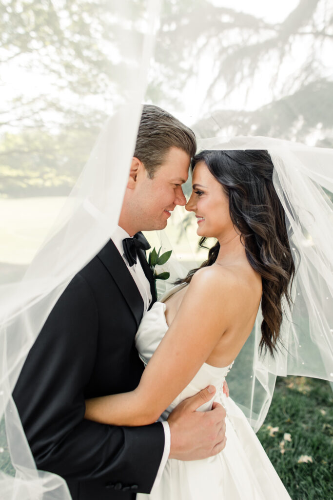 Bride, in white strapless dress, nose to nose with groom, in black suit, under white veil at Long View Country Club Wedding Venue Charlotte NC