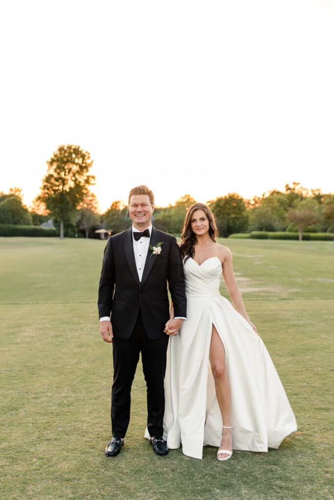 Bride, in white strapless dress, holding hands with groom, in black suit, on the golf course during golden hour at Long View Country Club Wedding Venue Charlotte NC