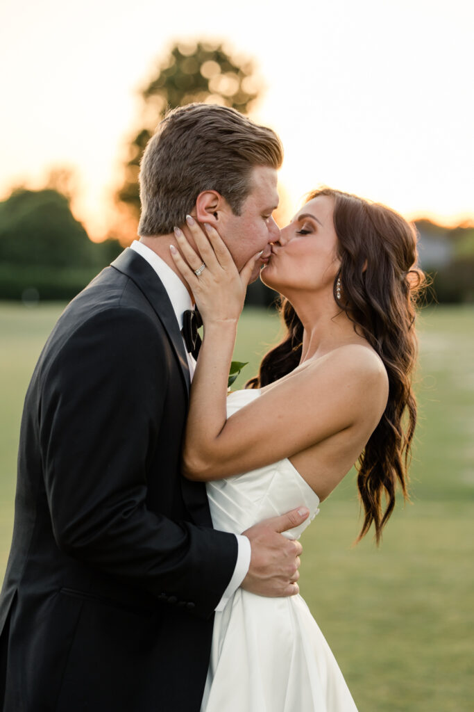 Bride, in white strapless dress, kissing groom, in black suit, on the golf course during golden hour at Long View Country Club Wedding Venue Charlotte NC