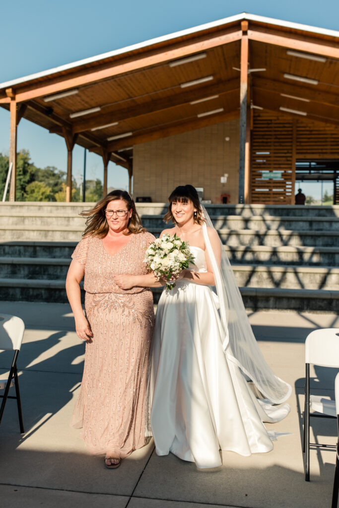 Bride, with short brown hair, wearing white strapless dress walking down isle with mother in champagne colored dress photographed by Charlotte Wedding Photographer
