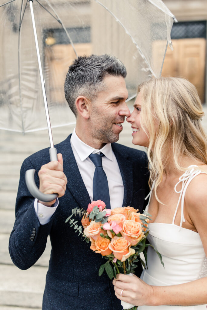 Bride with blonde hair and groom in navy suit smiling nose to nose under a clear umbrella. Photographed by Charlotte Wedding Photographer.