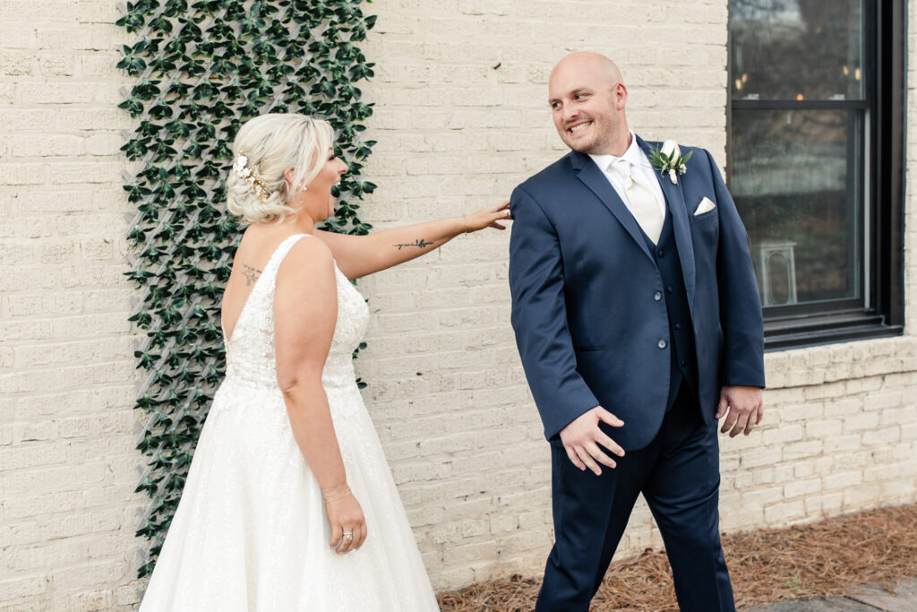 Bride with blonde hair in a white lace dress seeing her groom, in a navy suit for the first time at The Bottle Factory Wedding Venue. Photographed by Charlotte wedding photographer. 