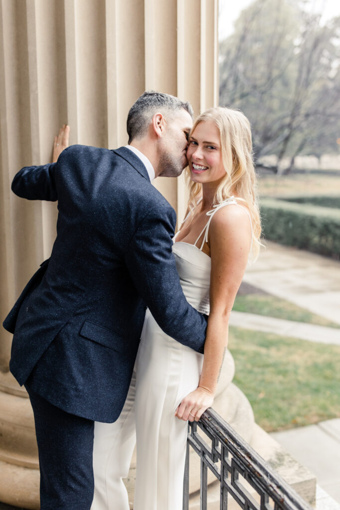 Groom, with grey hair in navy suit, kissing the cheek of blonde bride in uptown Charlotte NC. Photographed by Charlotte Wedding Photographer.
