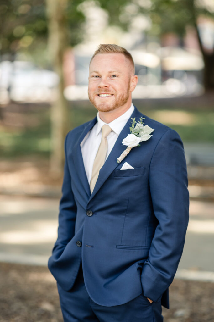 Groom smiling with blonde hair wearing a blue suit, gold tie and white boutonniere Photographed by Charlotte wedding photographer.
