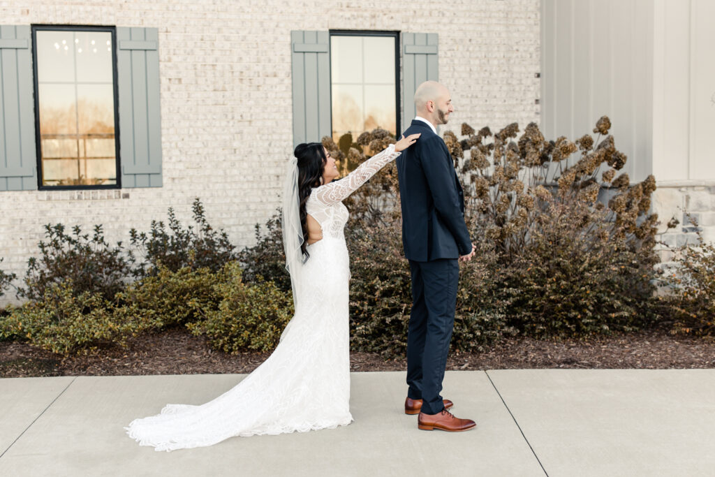 Bride in white long sleeve less dress and veil seeing her groom in blue suit for the first time at Fields at Skycrest Wedding Venue in Charlotte NC. Photographed by Charlotte wedding photographer.