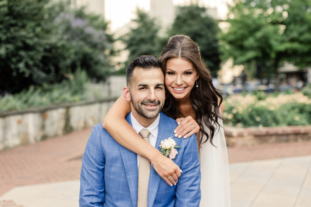 Bride in white dress with brown hair hugging and smiling with groom in blue suit in uptown Charlotte photographed by Charlotte Wedding Photographer.  