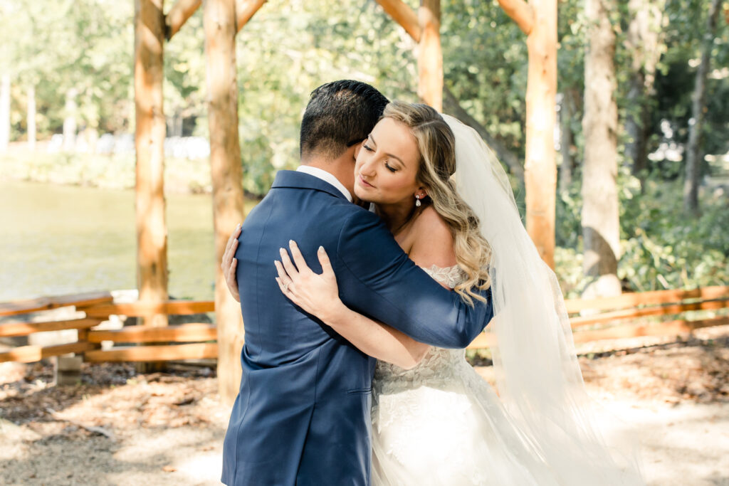 Bride with long blonde hair in a white lace dress hugging groom in blue suit at Riverwood Manor Wedding Venue. Photographed by Charlotte wedding photographer, Stephanie Bailey.