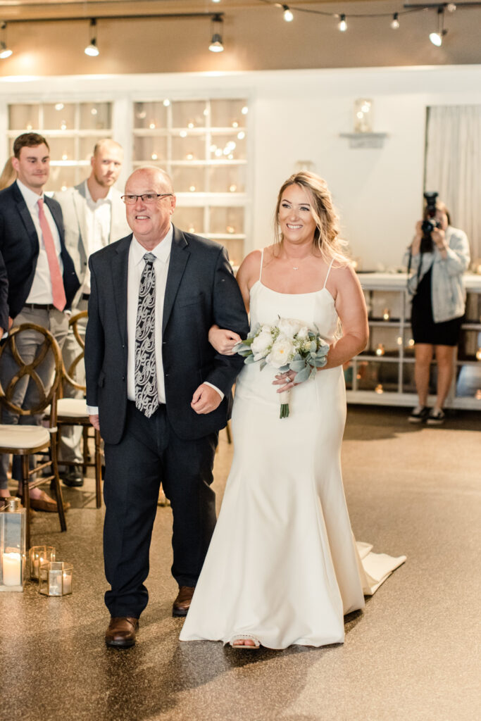 Bride with long blonde hair walking with father in black suit down the aisle at The Venue in Asheville NC during ceremony.  Photographed by Charlotte wedding photographer.