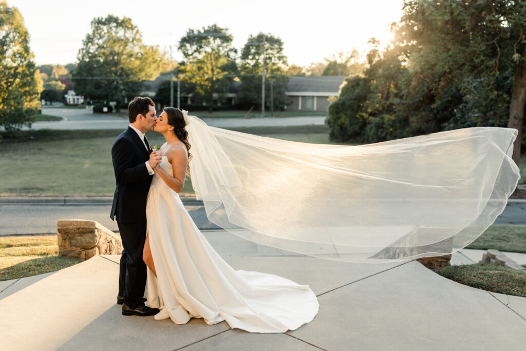 Bride with brown hair in a white strapless dress and long white veil kissing groom with brown hair in a navy suit at The Palmer Building Wedding Venue. Photographed by Charlotte Wedding photographer, Stephanie Bailey.