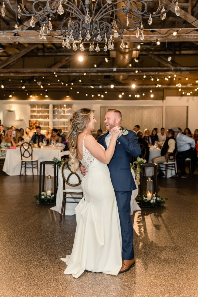 Bride in white dress with long blonde hair dancing with her groom in a blue suit during wedding reception at The Venue in Asheville NC. Photographed by Charlotte wedding photographer.