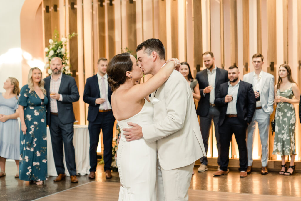 Bride, in white strapless dress, kissing her groom, in tan suit, during reception at The Ruth wedding venue in Charlotte NC. Photographed by Charlotte Wedding Photographer.