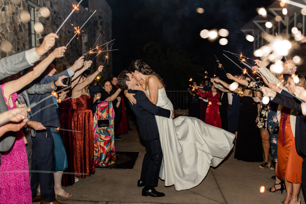 Bride with brown hair in a white strapless dress kissing groom with brown hair in a navy suit under under sparklers at The Palmer Building Wedding Venue. Photographed by Charlotte Wedding photographer, Stephanie Bailey.