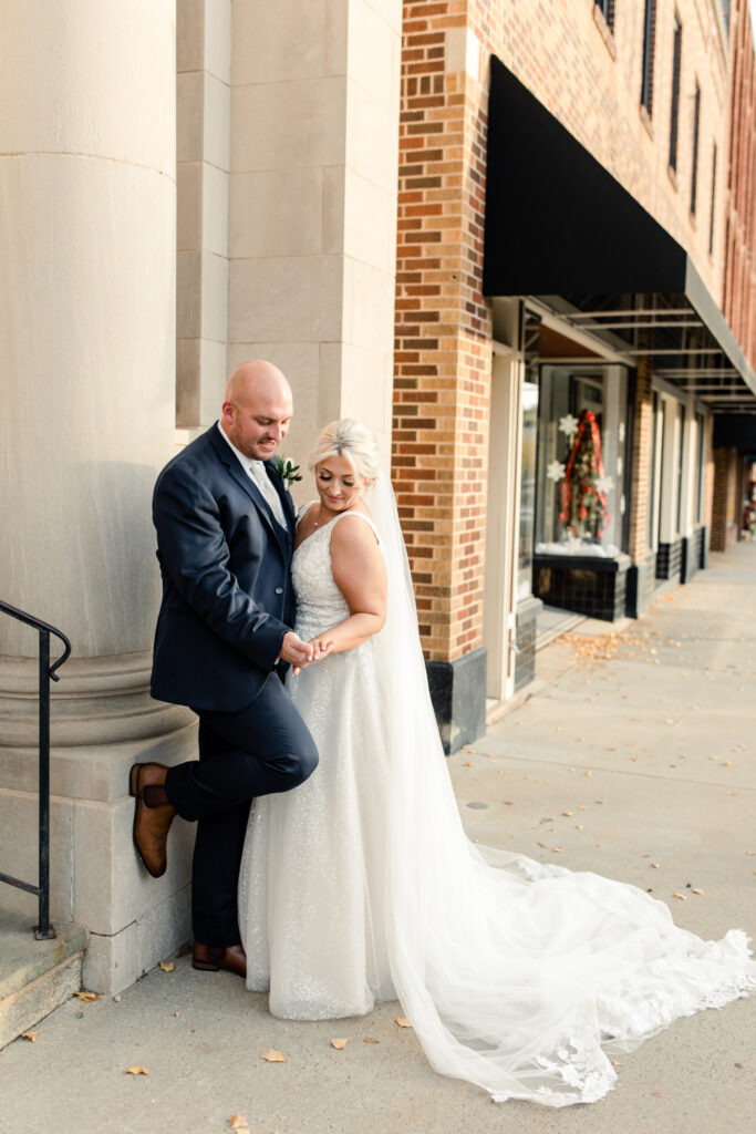 Bride with blonde hair in a white lace dress holding hands with groom, in a navy suit at The Bottle Factory Wedding Venue. Photographed by Charlotte wedding photographer. 