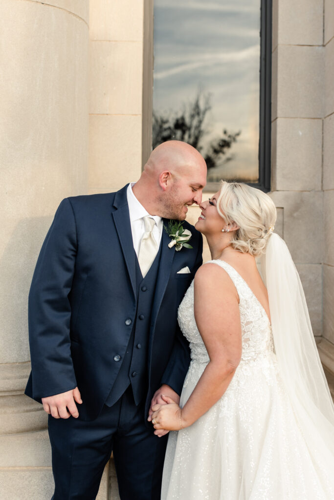 Bride with blonde hair in a white lace dress holding hands with groom, in a navy suit at The Bottle Factory Wedding Venue. Photographed by Charlotte wedding photographer. 