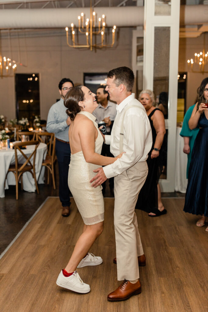 Bride, in white short dress, dancing with her groom, in tan suit, during reception at The Ruth wedding venue in Charlotte NC. Photographed by Charlotte Wedding Photographer.