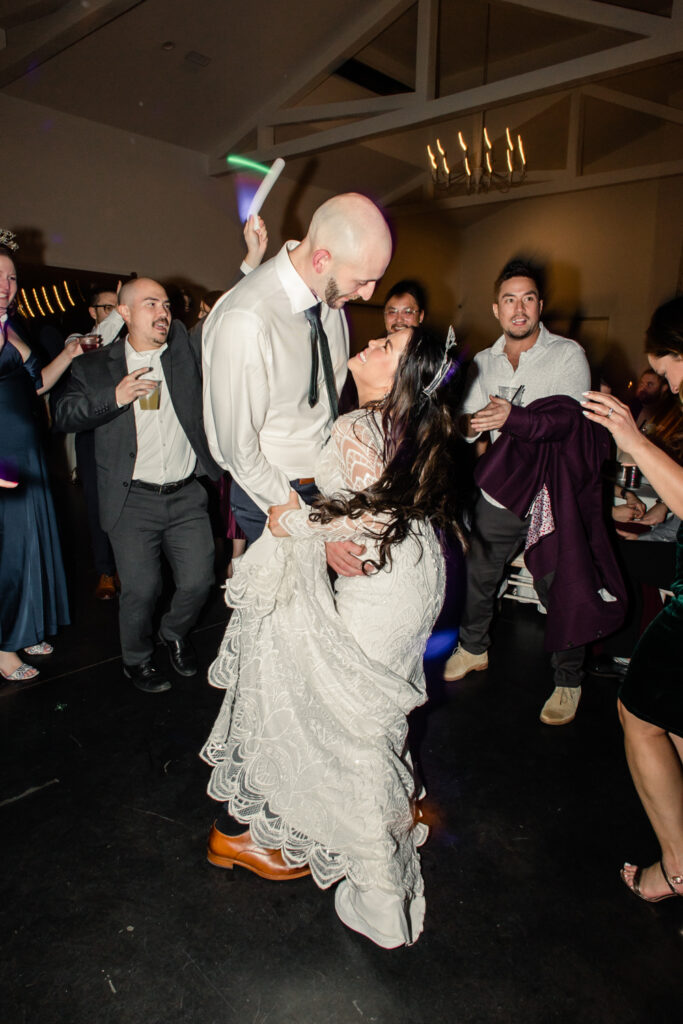 Bride with dark brown hair in a long white lace dress dancing with groom in white button down with green tie during reception at Fields at Skycrest Wedding Venue in Charlotte NC. Photographed by Charlotte wedding photographer.