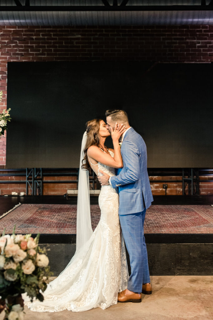 Bride in white dress and groom in blue suit kissing at ceremony photographed by Charlotte Wedding Photographer.  